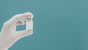 vaccine-bottle-held-by-hand-with-glove-copy-space_23-2148801397